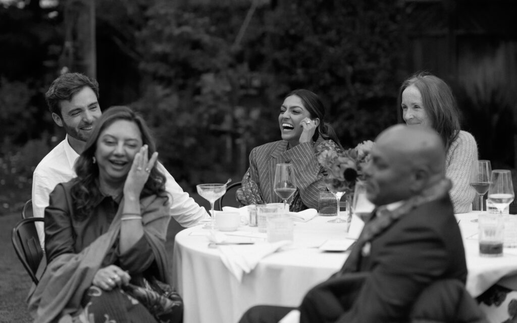 Family of the bride and groom laugh with the couple during their welcome dinner in California.