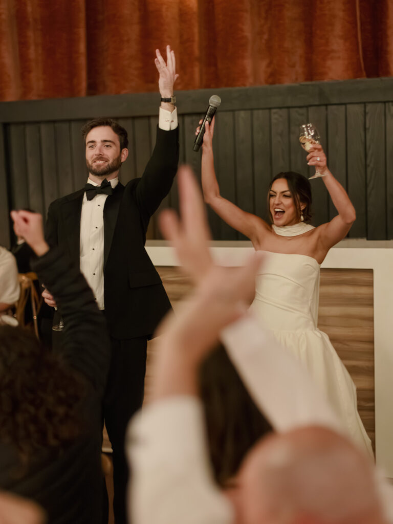 The wedding couple raise their hands to celebrate. 