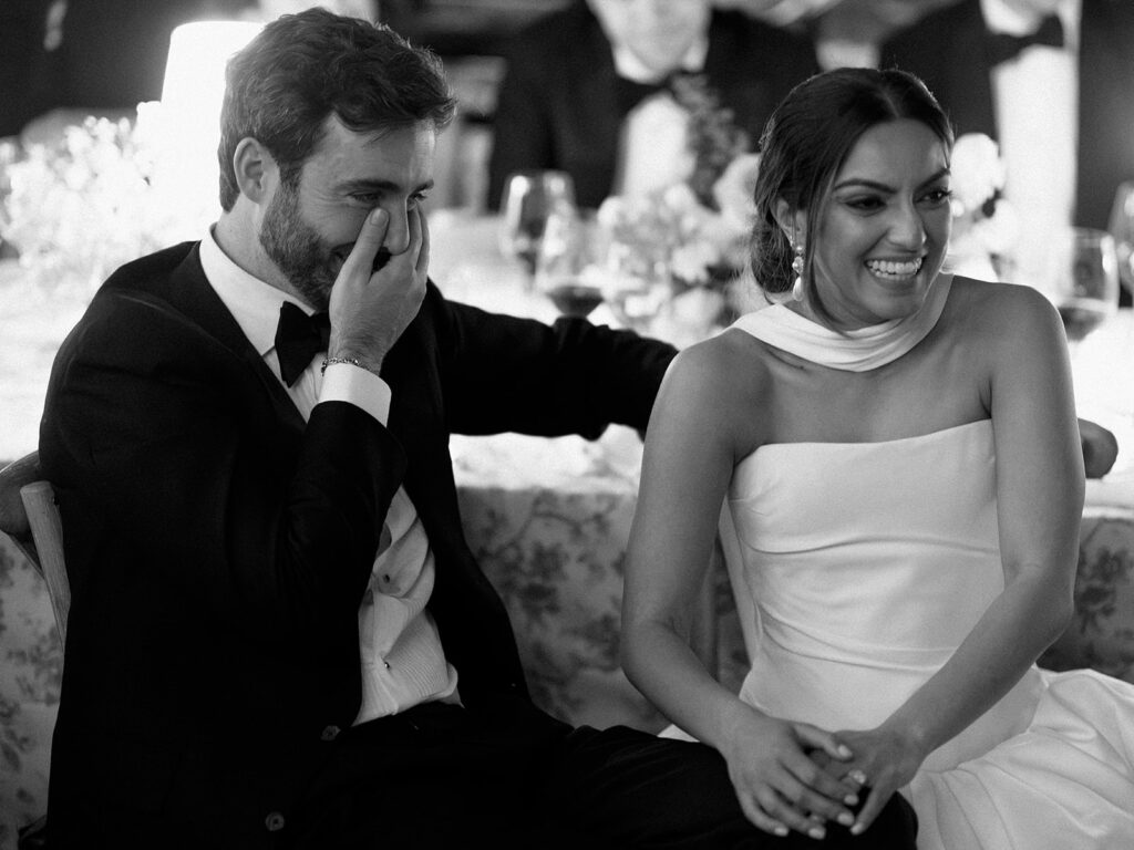 The bride and groom laugh together during their wedding reception with friends and family. 